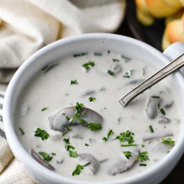 Close up shot of a spoon in a white bowl of cream of mushroom soup with fresh herbs on top