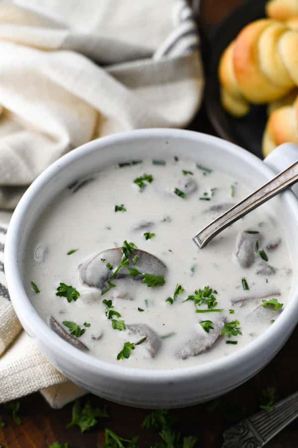 Close up shot of a spoon in a white bowl of cream of mushroom soup with fresh herbs on top
