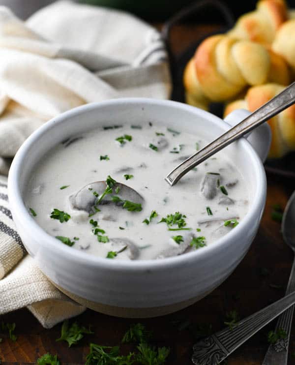 Spoon in a bowl of creamy mushroom soup with rolls in the background