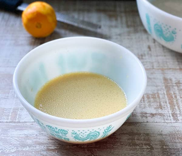 Wet ingredients for easy orange muffins mixed together in a white mixing bowl.
