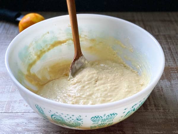A bowl of orange muffin batter, mixed together with a wooden spoon.