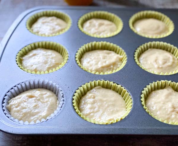 A metal muffin tin filled with cups of unbaked orange muffin batter.
