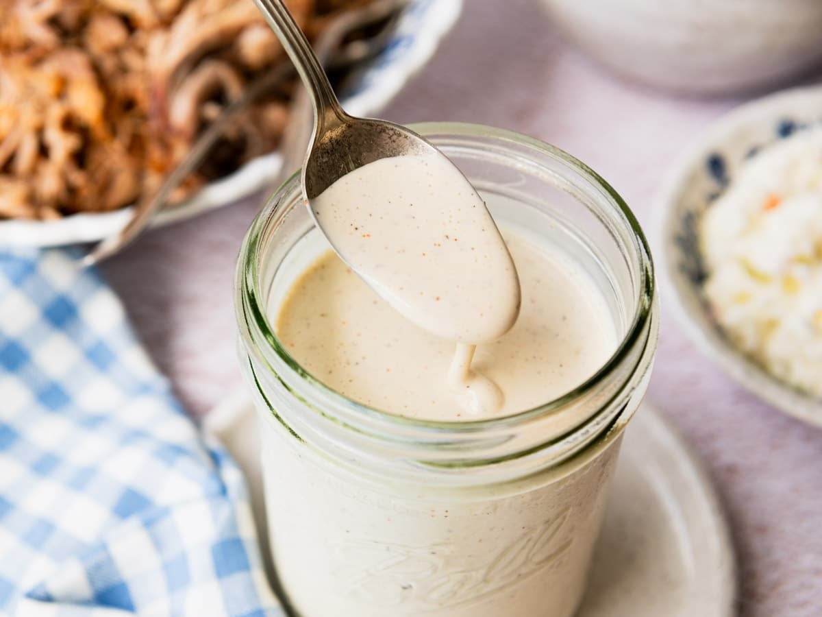 Horizontal side shot of a spoon in a jar of Alabama white bbq sauce.