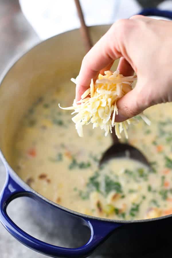 Adding grated sharp cheddar cheese to a pot of creamy cauliflower soup