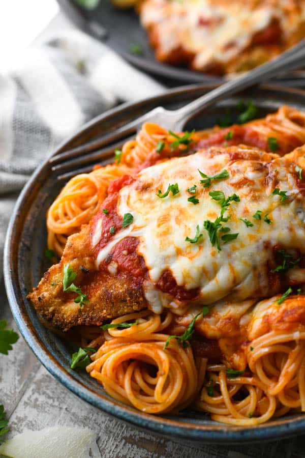 The best chicken parmesan recipe garnished with fresh parsley and served over spaghetti