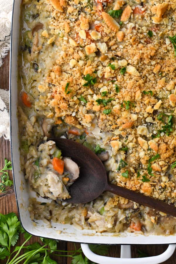 Close overhead image of a wooden spoon in a dish of creamy chicken and wild rice casserole