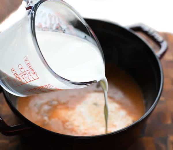 Pouring heavy cream from a Pyrex measuring cup into a cast iron soup pot. 