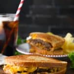 Patty melt sandwich on a cutting board with soda in the background