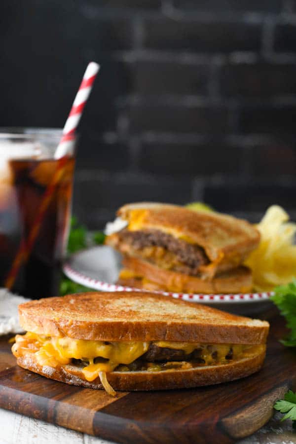 Patty melt sandwich on a cutting board with soda in the background