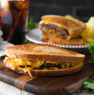Square side shot of a patty melt on a wooden cutting board