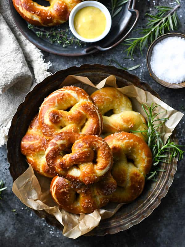 Overhead image of a round tray of soft baked pretzels on a table with mustard and salt