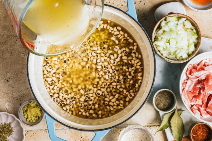 Pouring broth into a Dutch oven of black eyed peas.