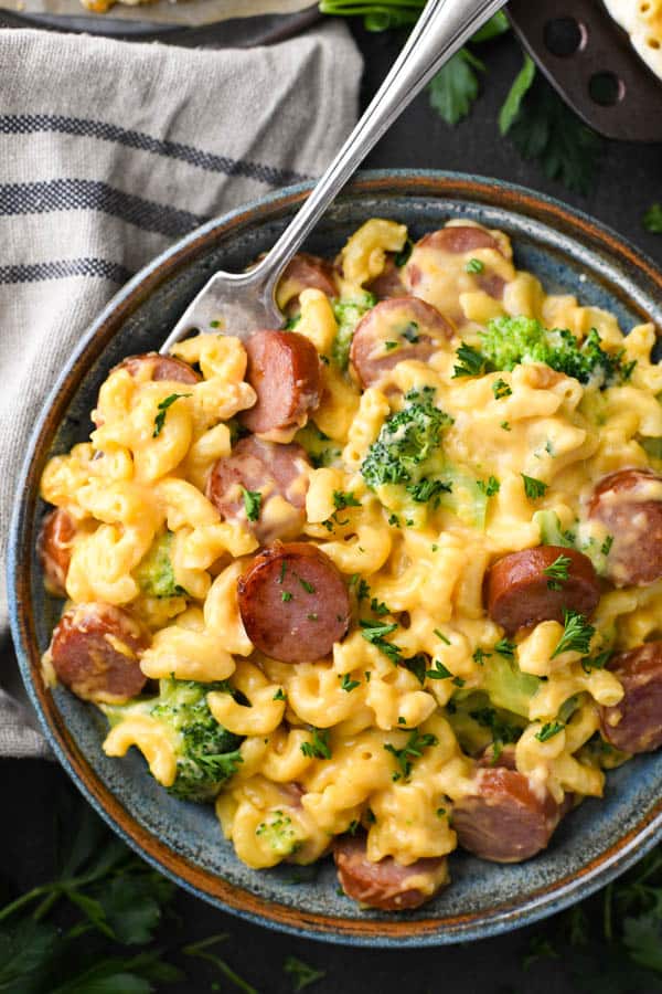 Close overhead shot of a blue bowl full of cheesy smoked sausage pasta with broccoli