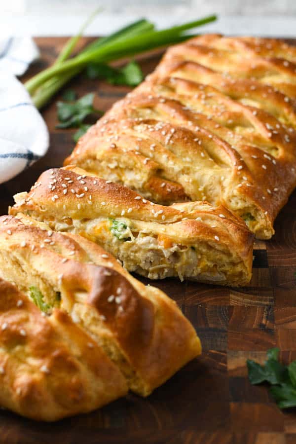 Front shot of braided chicken pastry on a cutting board with parsley and green onions nearby