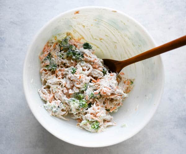 Overhead shot of chicken and broccoli filling in a white mixing bowl with wooden spoon
