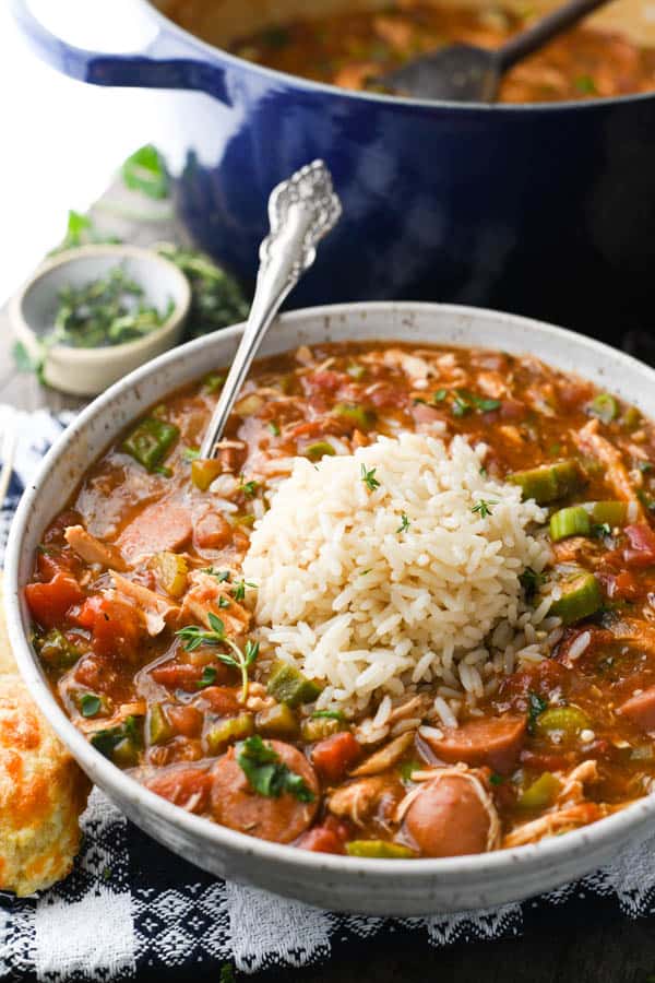 A close up image of a bowl of chicken and sausage gumbo. The soup is topped with a scoop of white rice in the center. 
