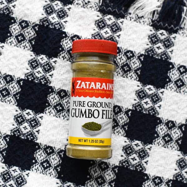 A small bottle of Zatarains pure ground gumbo file powder is pictured on a black and white checkered table cloth.