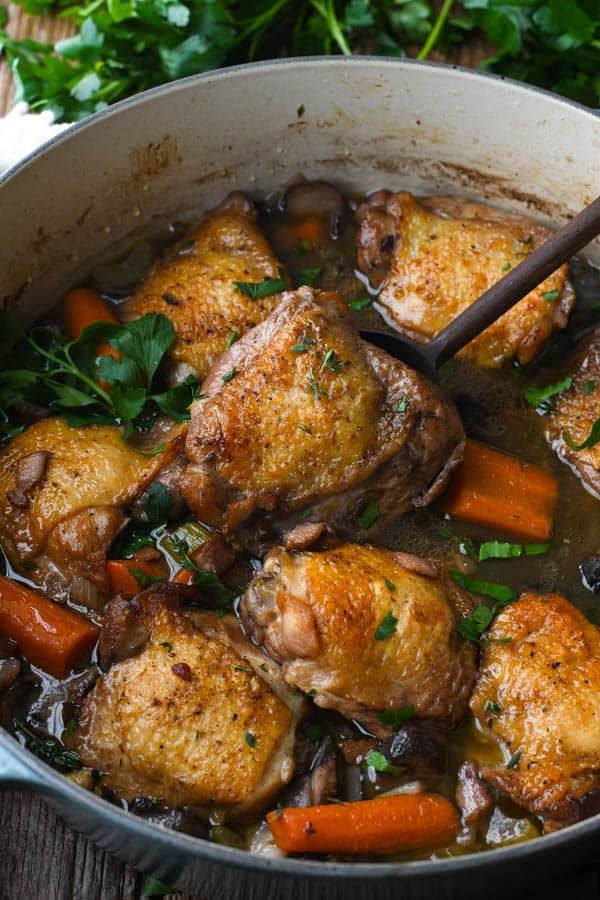 Close up shot of a wooden spoon in a pot of coq au vin