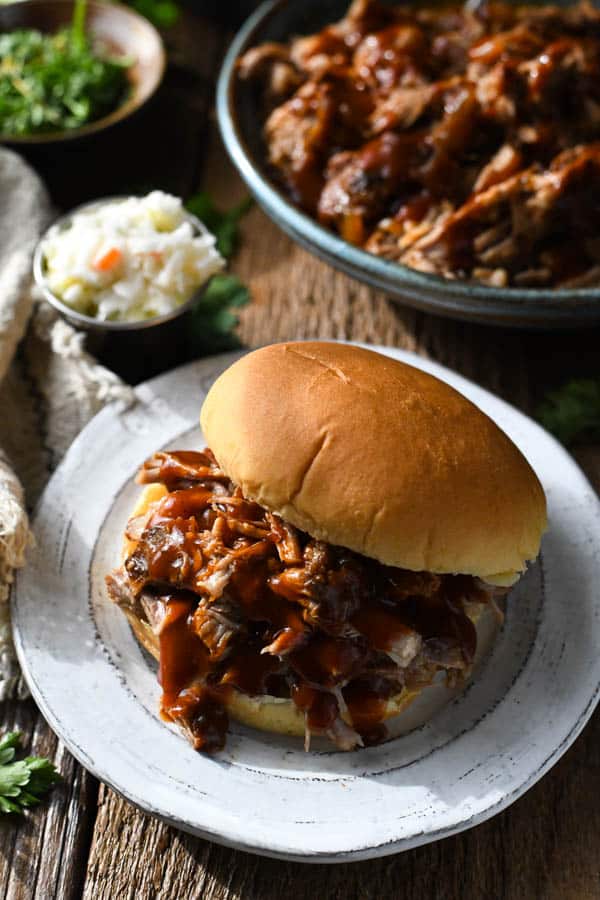 Dr. Pepper pulled pork recipe served on a sandwich bun on a white plate