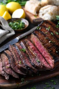 Marinated london broil on a cutting board with fresh herbs