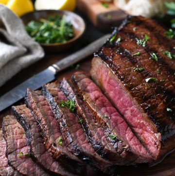 Marinated london broil on a cutting board with fresh herbs
