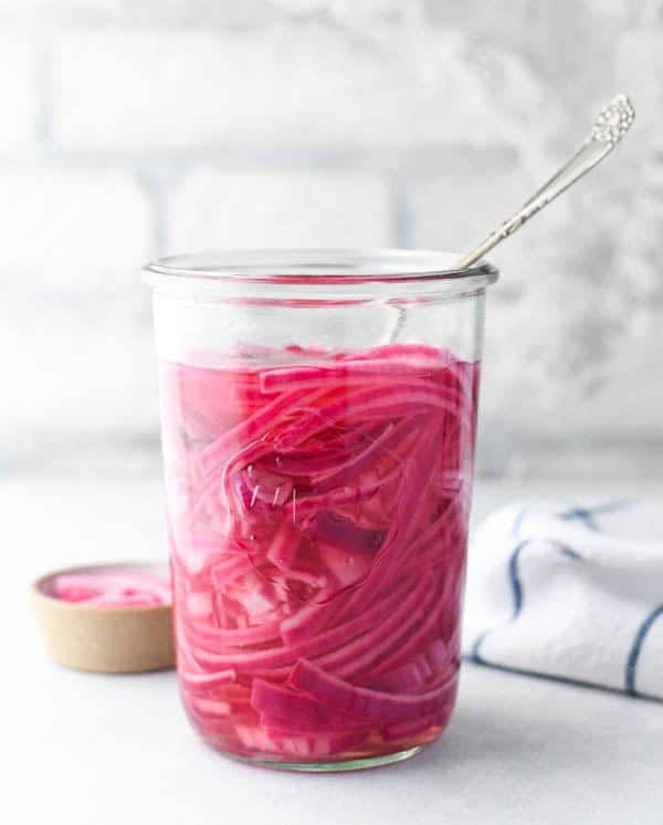 Front shot of a jar of pickled red onions in front of a white wall
