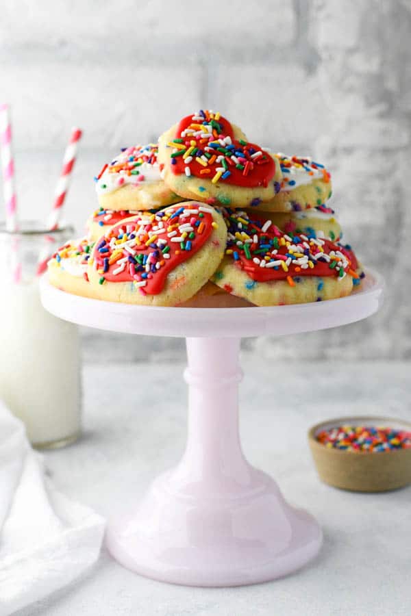 Side shot of a pink cake stand full of sugar cookies with sprinkles