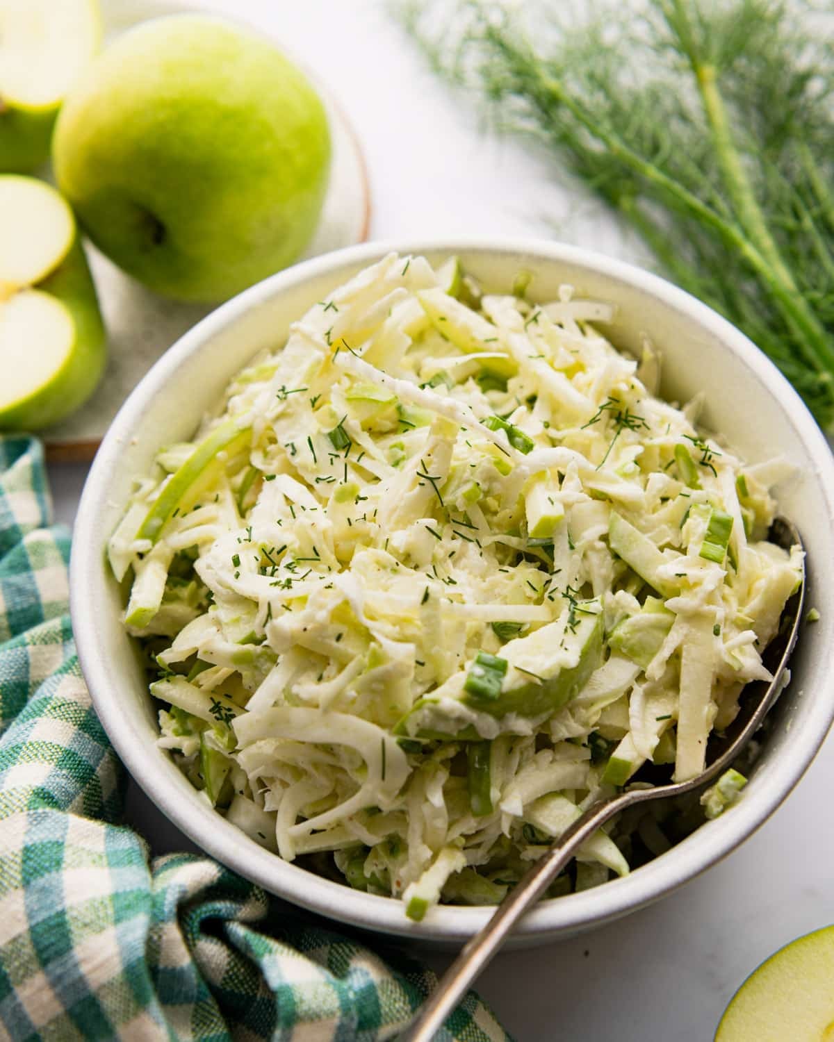 Side shot of fennel and apple salad with creamy cider dressing in a white bowl.