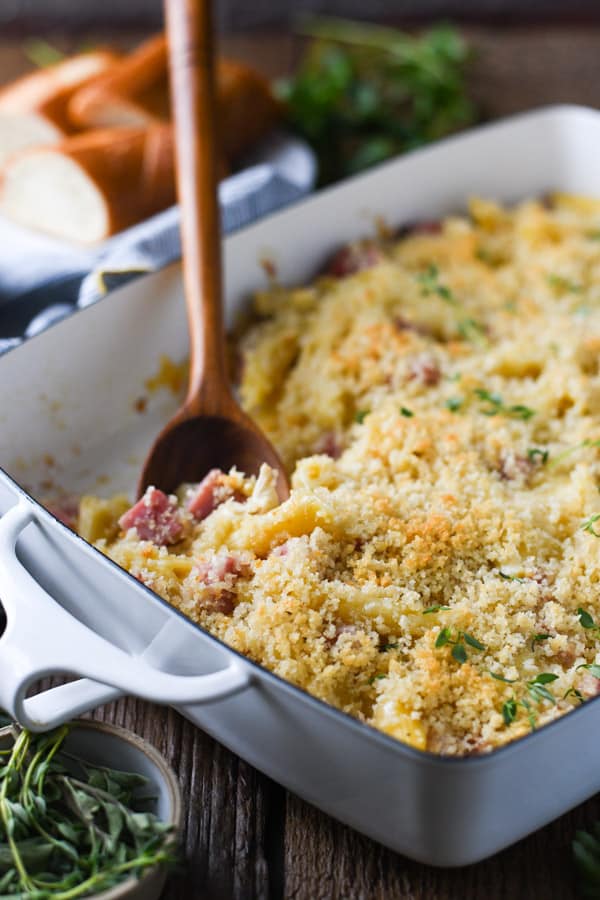 A white casserole dish of chicken cordon bleu casserole, made with pasta, chicken and ham in a creamy sauce, topped with breadcrumbs.