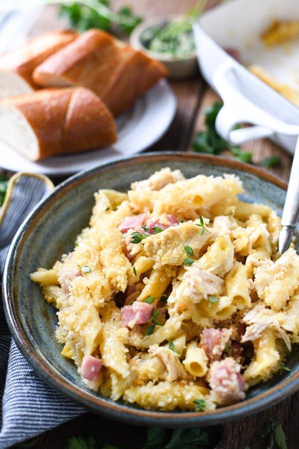 A bowl of creamy chicken cordon bleu pasta casserole, made with penne pasta, ham, and chicken, served in a bowl with a silver fork.