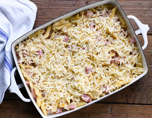 A casserole dish of mixed chicken cordon bleu ingredients, topped with shredded mozzarella cheese, ready to be baked.