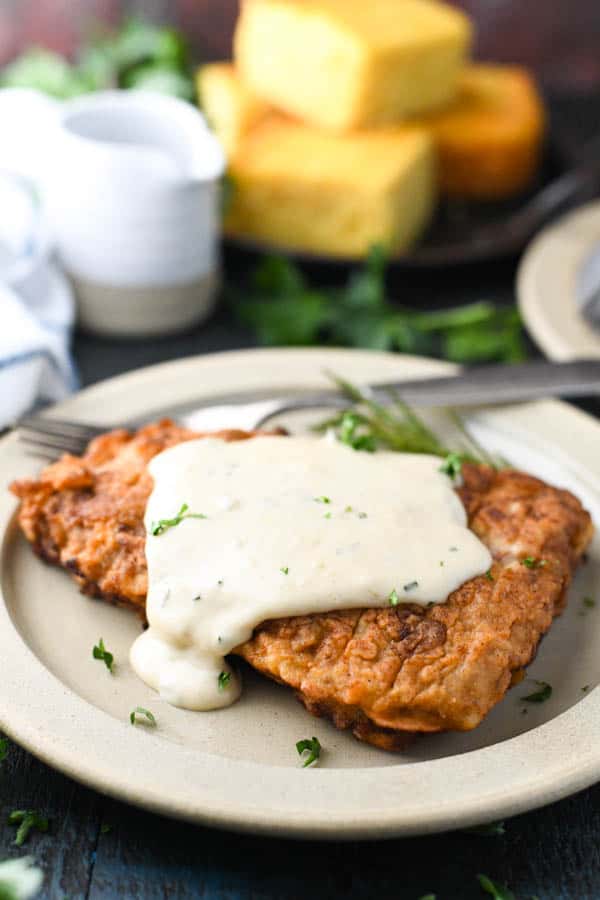 Side shot of the best chicken fried steak recipe on a plate with cornbread in the background