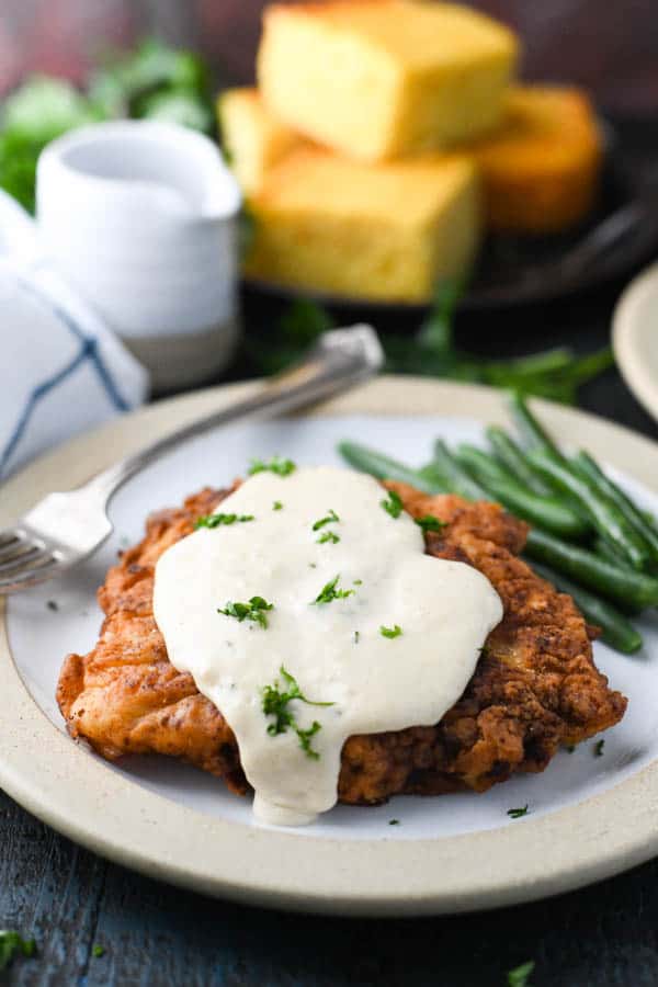 Side shot of easy chicken fried steak on a plate with green beans and cornbread