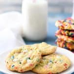 Side shot of a white plate full of funfetti chip cookies