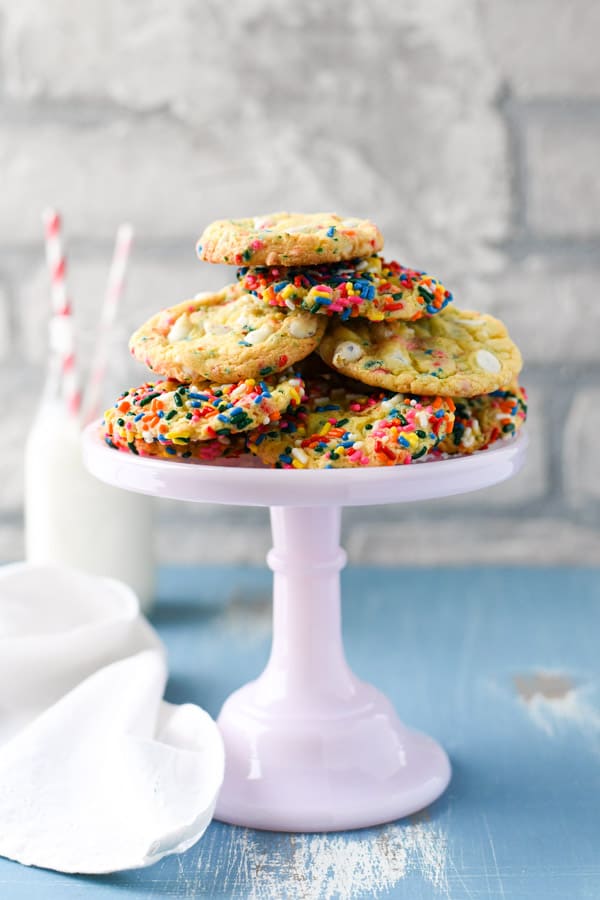 Funfetti cake mix cookies stacked on a white cake stand. There are cookies covered in sprinkles and cookies stilled with funfetti chips.