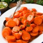 Close up front shot of glazed carrots on a white serving tray with parsley garnish