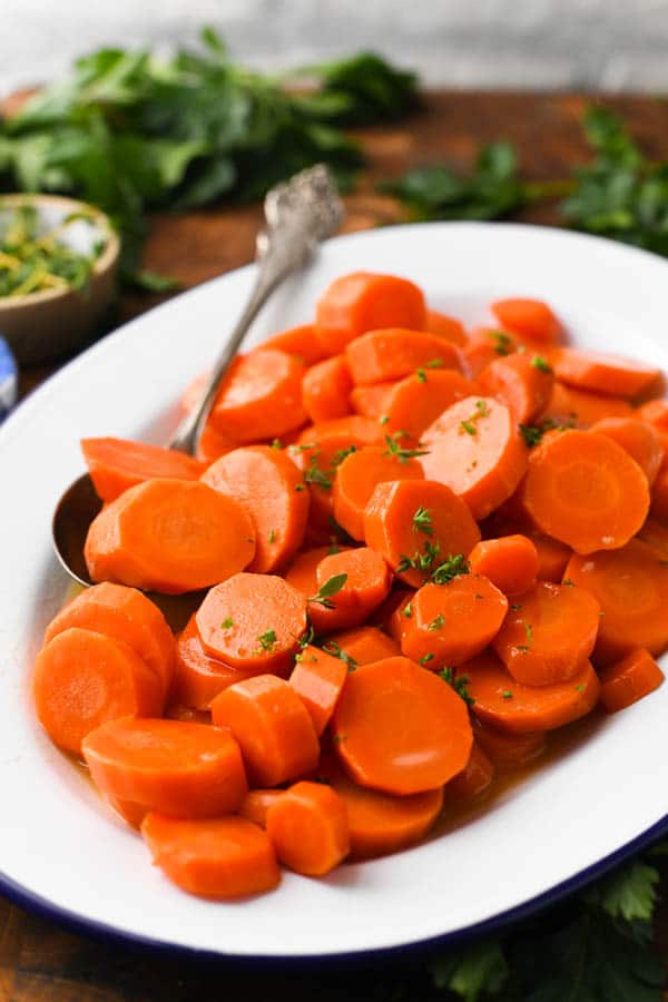 Close up front shot of glazed carrots on a white serving tray with parsley garnish