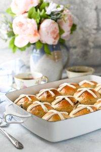 Side shot of the softest hot cross buns recipe on a white table in front of a vase of flowers