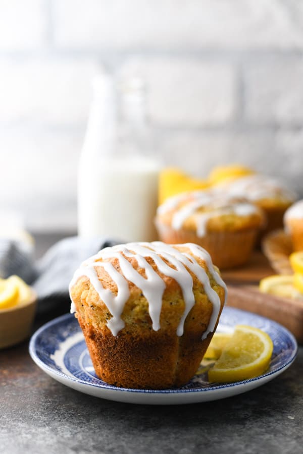 Side shot of a tall, puffy, easy lemon poppy seed muffin recipe with a high dome on a blue and white plate