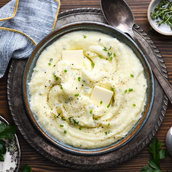 Square overhead shot of a bowl of creamy mashed potatoes with sour cream and chives on a wooden table