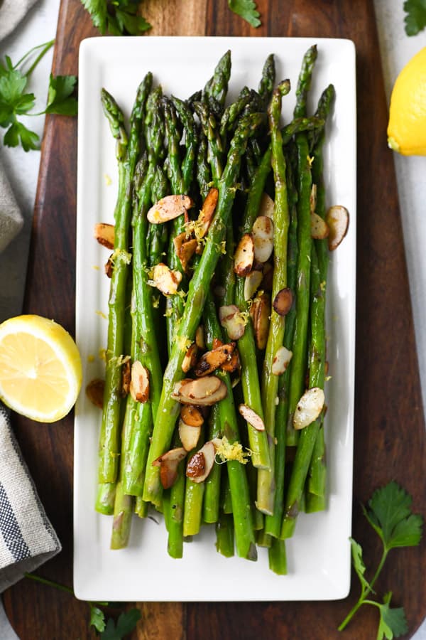 Overhead image of sauteed asparagus with lemon and garlic on a white serving dish.