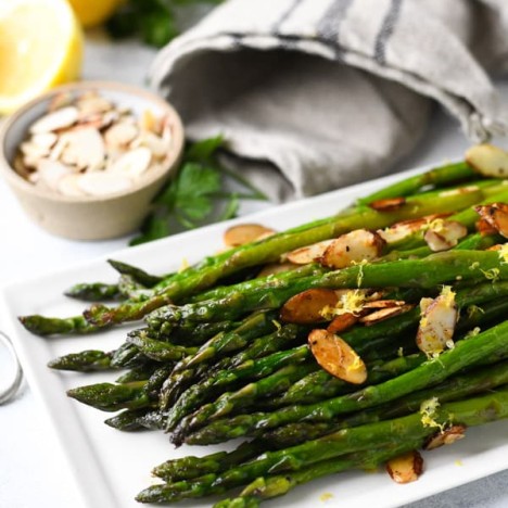 Close up side shot of sauteed asparagus with lemon and garlic on a white serving tray with toasted almonds on top