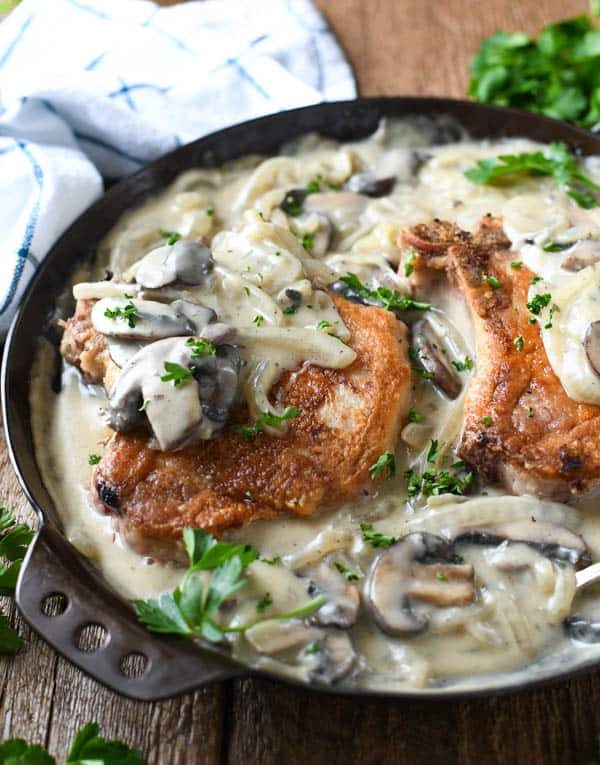 Side shot of pork chops in a skillet with creamy mushroom and onion gravy