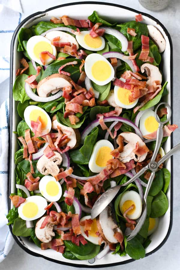 Long overhead shot of a bowl of spinach salad with bacon and poppy seed dressing