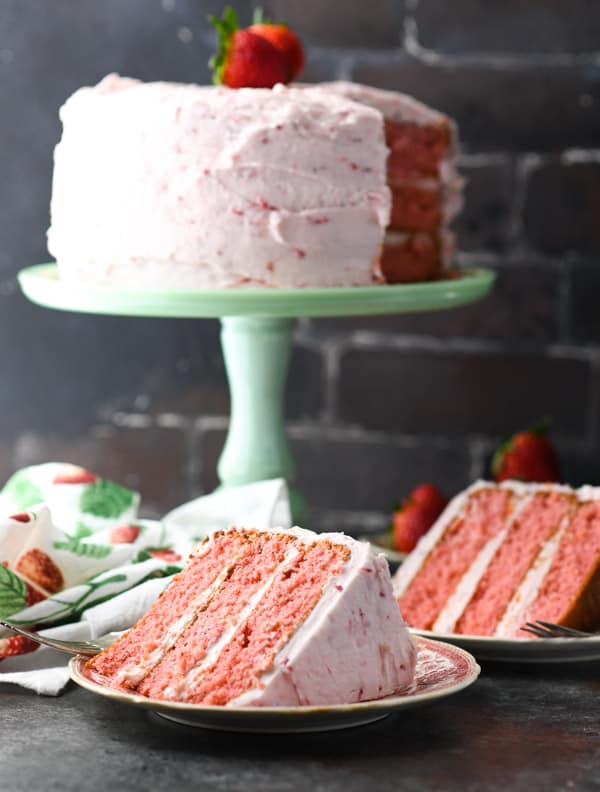 Side shot of a strawberry cake with cream cheese frosting in front of a brick wall