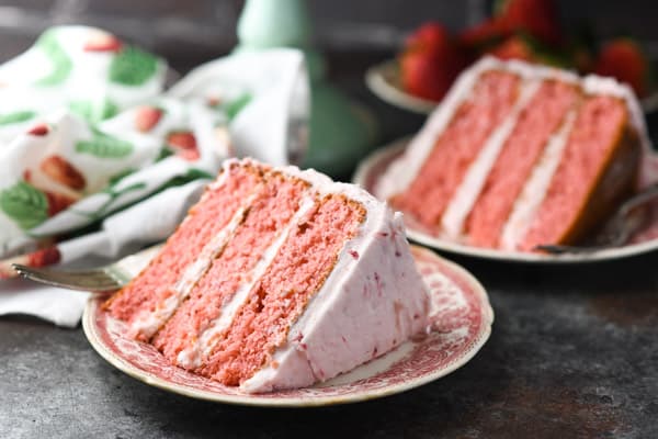 Horizontal shot of two pieces of the best strawberry layer cake on red and white serving plates
