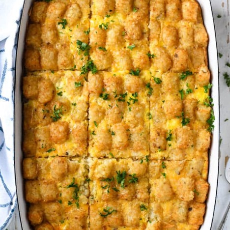 Overhead image of tater tot breakfast casserole with sausage in a white baking dish on a white table