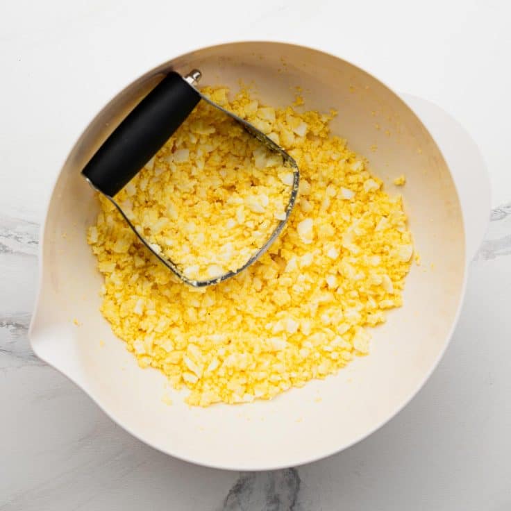 Chopping hard boiled egg in a bowl.