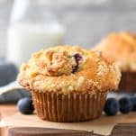 Close up side shot of blueberry muffins with crumb topping on a wooden cutting board