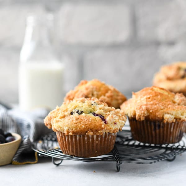 Square image of a blueberry streusel muffin recipe cooling on a wire rack